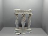 une statue représentant trois femmes tenant un panier posé sur une table