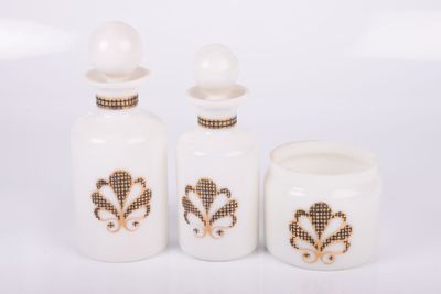 three white glass bottles with gold designs on them on a white surface