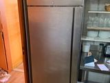 un réfrigérateur en acier inoxydable dans une cuisine où une étagère est remplie de vaisselle