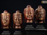 quatre têtes de Bouddha en bois posées sur des socles, sur fond noir
