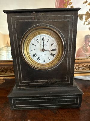 a small clock sitting on a table with a picture in the background
