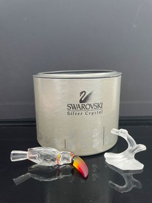 un récipient en argent orné d'un poisson, à côté d'une paire de cuillères en plastique