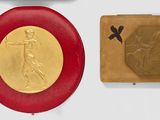 two gold medals and a red plaque on a white surface