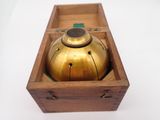 une cloche ancienne en laiton, posée dans une boîte en bois sur une surface blanche