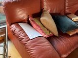 a brown leather couch with pillows and a book on it