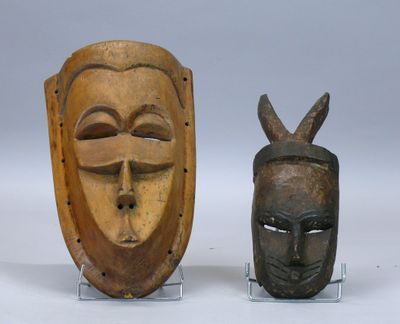 Deux masques en bois sont posés sur un socle, sur une surface blanche.