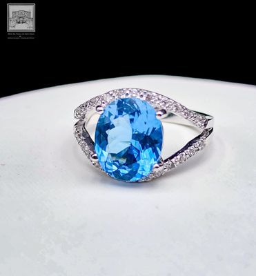 an oval blue topaze and diamond ring sitting on a white surface