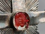 silver cross with a red wax seal on top of it