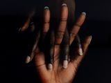 woman ' s hands with black nails and white manicures against a black background