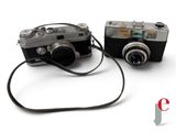 two cameras sitting next to each other on a white surface