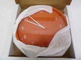 a large orange clock in a box with a plastic cover