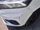 the front end of a white car with a dent in it