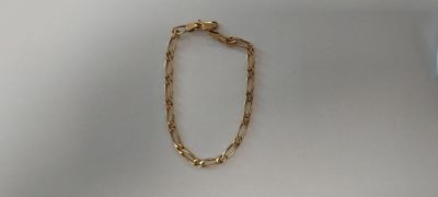 Le bracelet en chaîne d'or est exposé sur une surface blanche