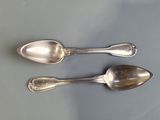 two silver spoons sitting on a table next to each other