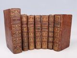 six old books are lined up in a row on a white surface