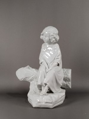 une figurine blanche représentant un garçon assis sur un rocher avec un poisson