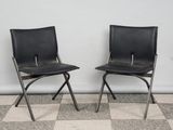 pair of black leather folding chairs against a white wall with checkered floor