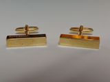 two gold cufflinks on a white surface with a white background