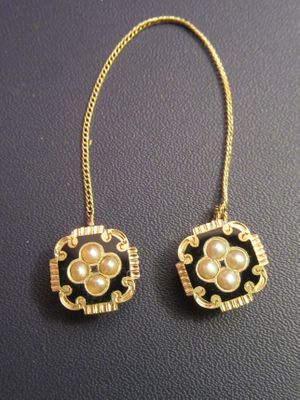 pair of earrings with pearls and gold chains on a black surface