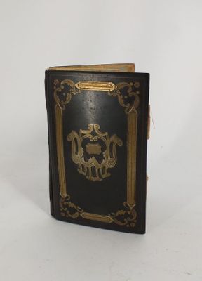 un vieux livre noir aux tranches dorées posé sur une surface blanche