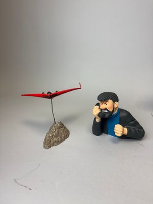 une figurine représentant un homme assis sur un rocher à côté d'un petit avion