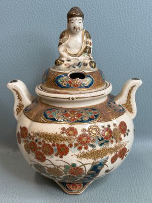 a small teapot with a buddha on it