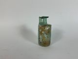 a small green glass bottle with a handle on a white surface