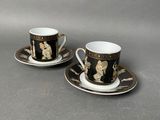 two cups and saucers with black and gold designs on them