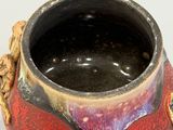 a red and black vase with a gold handle on a table