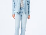 a woman wearing a denim shirt and jeans stands in front of a white background