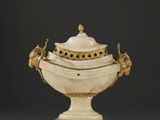 un vase blanc et doré muni d'un couvercle, posé sur une table