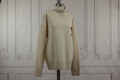 beige turtle neck sweater on a mannequin stand in front of a white paneled wall
