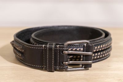 ceinture en cuir noir avec des boucles argentées posée sur une surface en bois