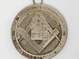 une image représentant une médaille d'argent sur laquelle figure un symbole maçonnique