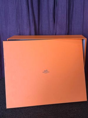 une boîte orange posée sur un tapis noir, à côté d'un rideau violet