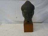 une photo représentant une statue représentant une tête posée sur un socle en bois