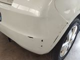 the rear end of a white car with a dent in it