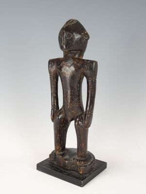 une statue en bois représentant un homme debout, les mains dans les poches