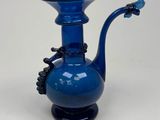 a blue glass vase with a black handle on a table