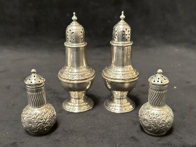 trois salières et poivrières en argent posées sur une surface noire