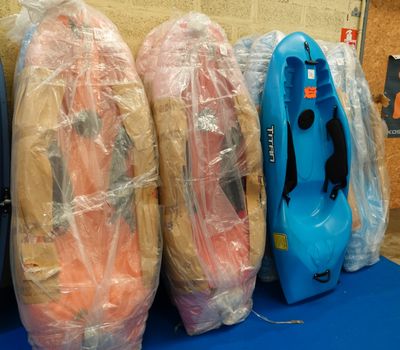 trois kayaks emballés dans du plastique, posés sur une table bleue