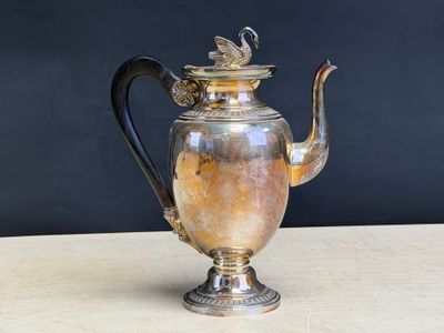 an antique silver tea pot with a black handle on a wooden table
