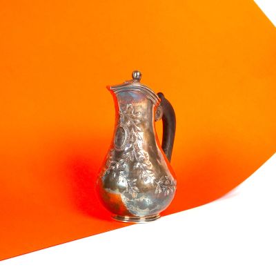 un pichet en argent posé sur un support orange