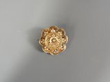 une image représentant une broche en forme de fleur dorée posée sur une surface grise