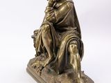 an antique bronze statue of a man sitting on a rock