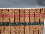 six old books are lined up in a row on a gray surface