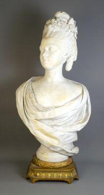 un buste de femme en marbre blanc posé sur un socle en or