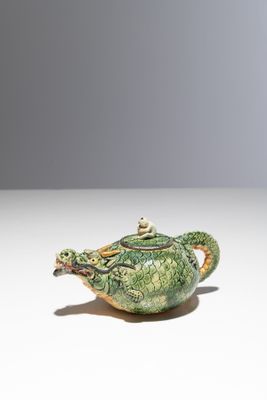 une image représentant une théière verte et dorée posée sur une surface blanche
