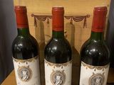 three bottles of red wine sit on a table next to a wooden box