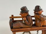 two wooden figurines of two men sitting on a bench